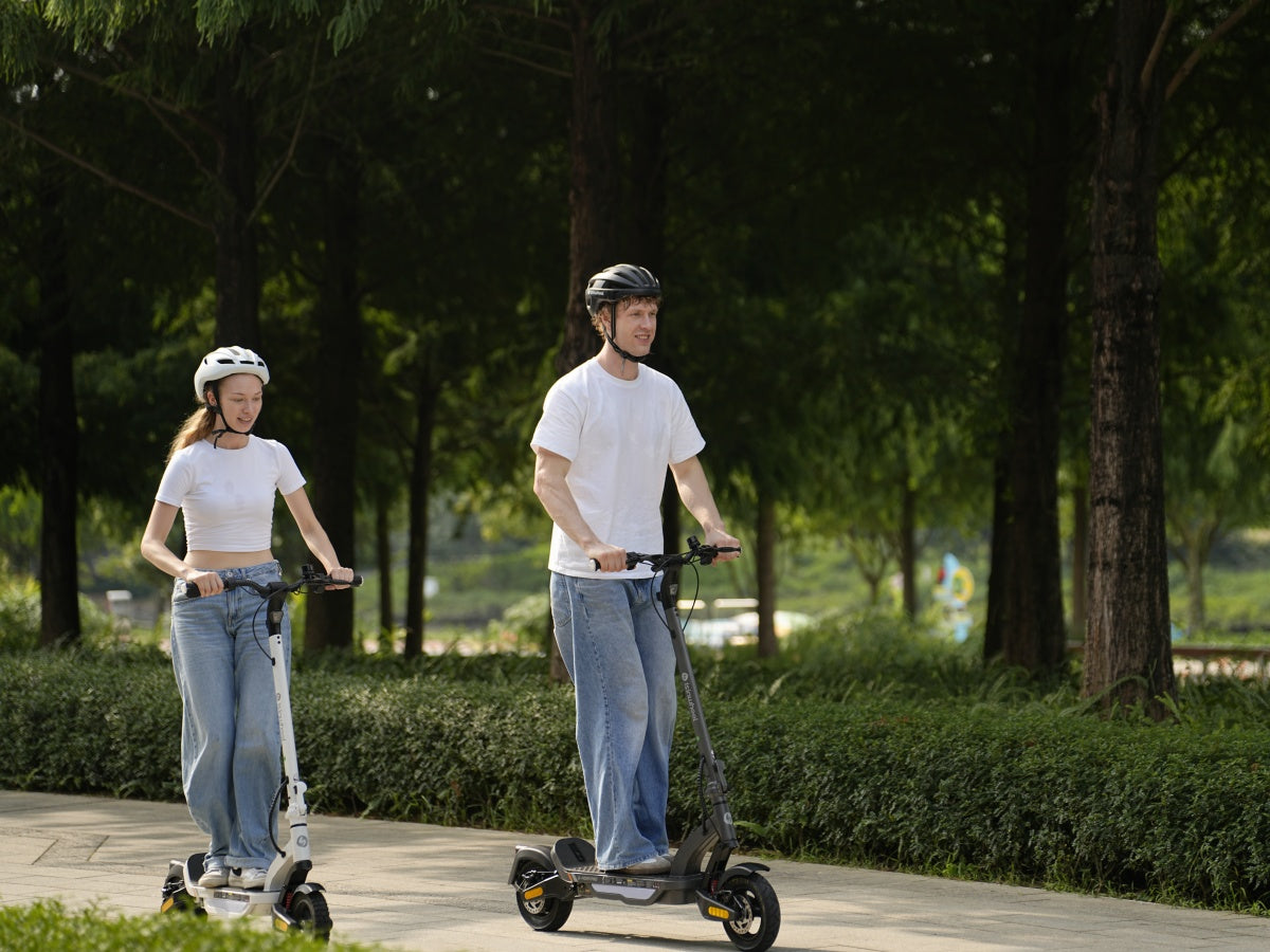 Two riders on iSinwheel S Nova scooters on a green park road