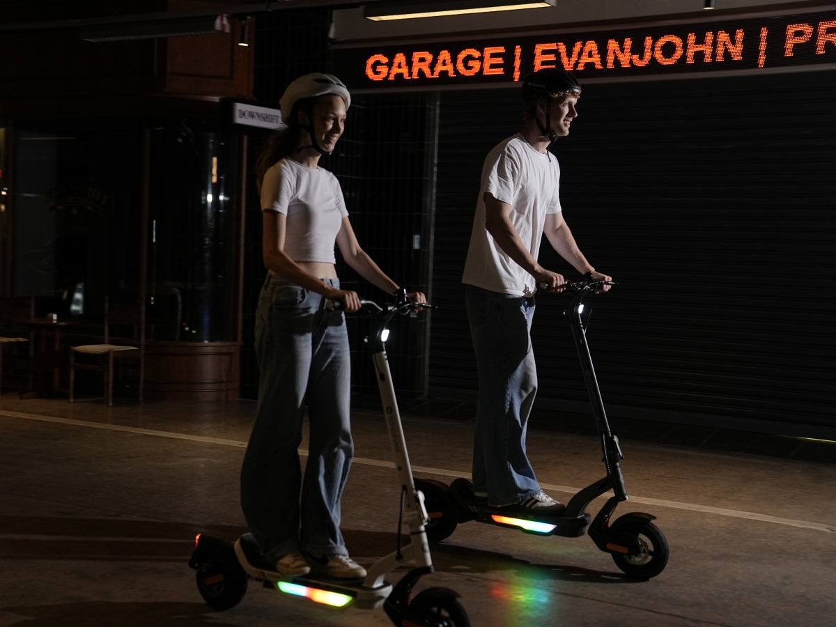 Two riders on iSinwheel S Nova scooters at night with the deck lights on